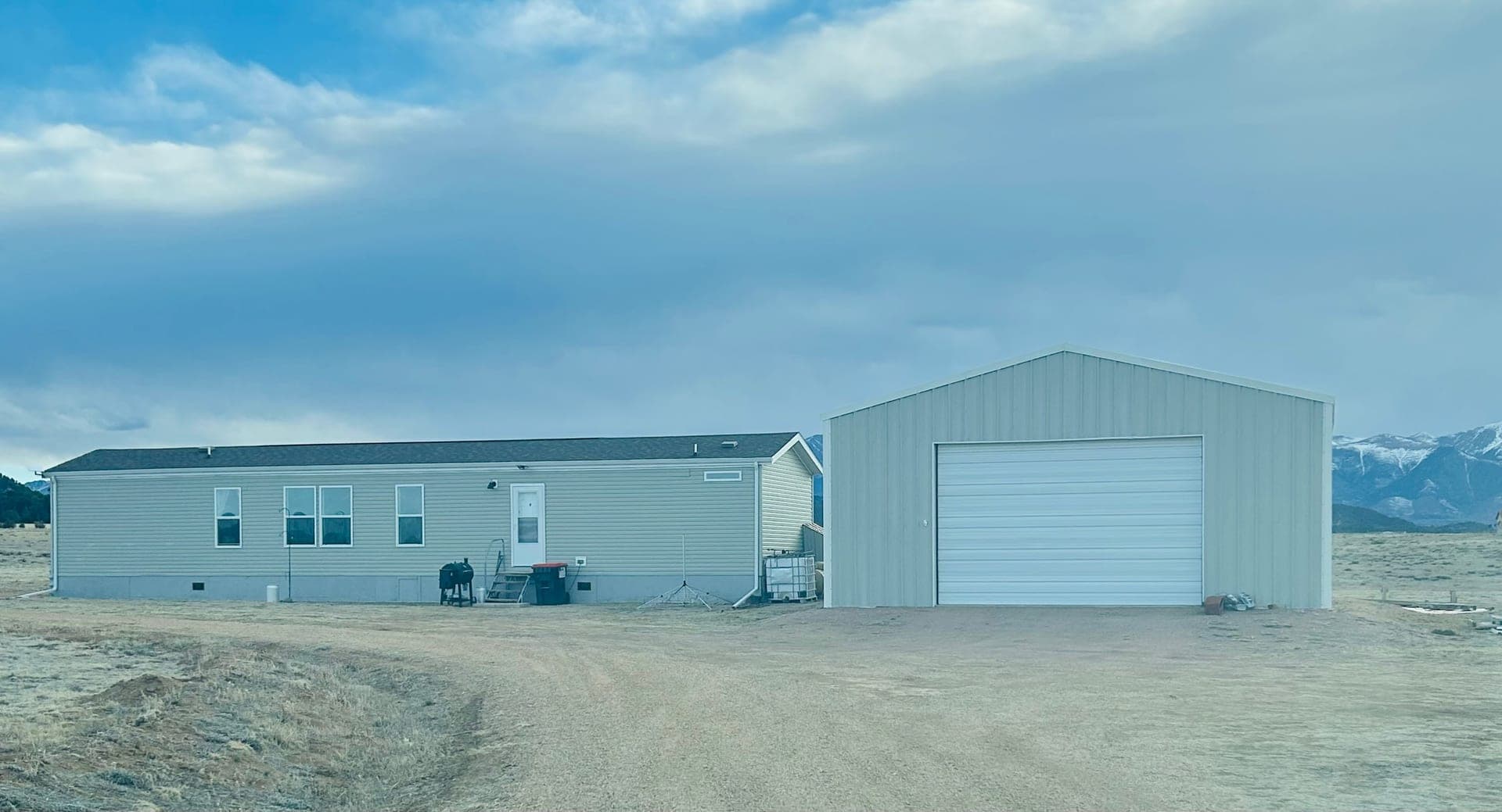 Finished white steel garage and shop with a metal gable roof set against the mountains in Cotopaxi, Colorado